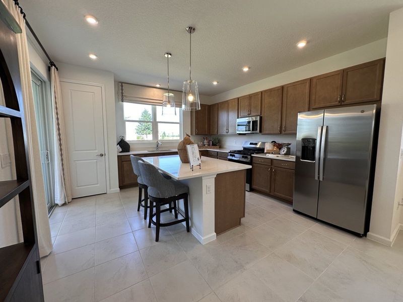 A modern kitchen with wooden cabinets, a central island, stainless steel appliances, and sleek lighting.
