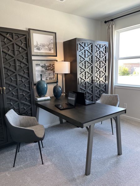 A modern home office with elegant dark furniture, decorative cabinets, and ample natural light.