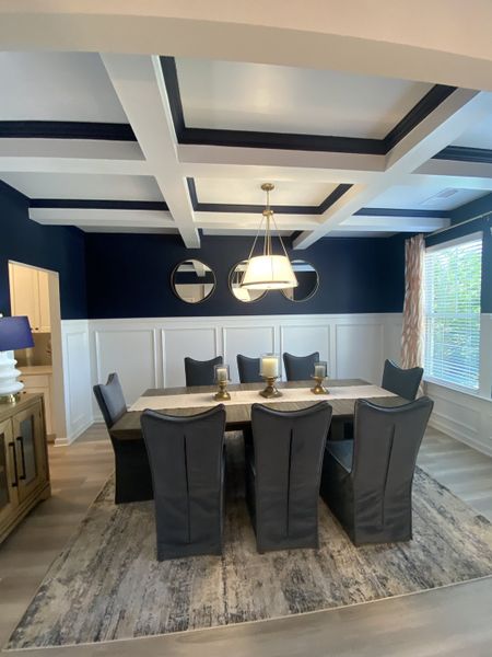 Elegant dining room with dark blue walls, coffered ceiling, and sleek furnishings, featuring a modern chandelier and stylish decor.