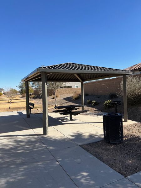 A community area with a metal pavilion, picnic table, and trash bin in Tortosa by KB Home (Maricopa, AZ).