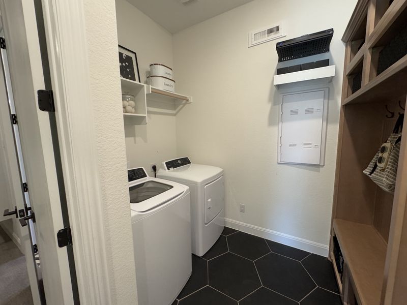 A modern laundry room featuring a washer, dryer, and sleek shelving on hexagonal tiled floors. A modern laundry room featuring a washer, dryer, and sleek shelving on hexagonal tiled floors.