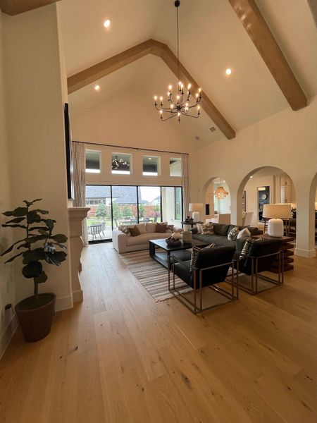 A spacious living room with vaulted ceilings, wood beams, a grand chandelier, and plush seating, offering a warm, inviting ambiance.
