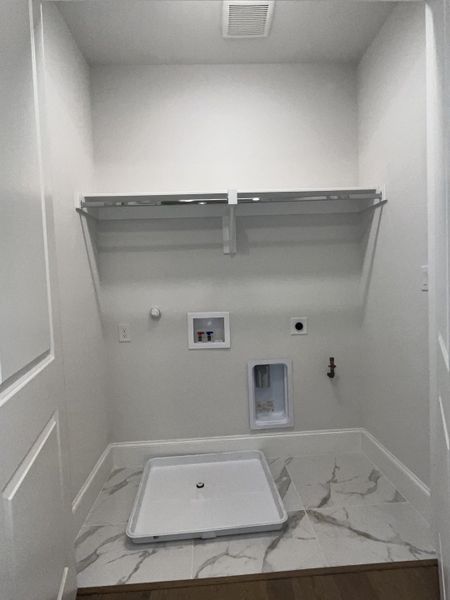 A sleek laundry space with white shelving, marble-patterned floor tiles, and modern hookups for convenience. A sleek laundry space with white shelving, marble-patterned floor tiles, and modern hookups for convenience.