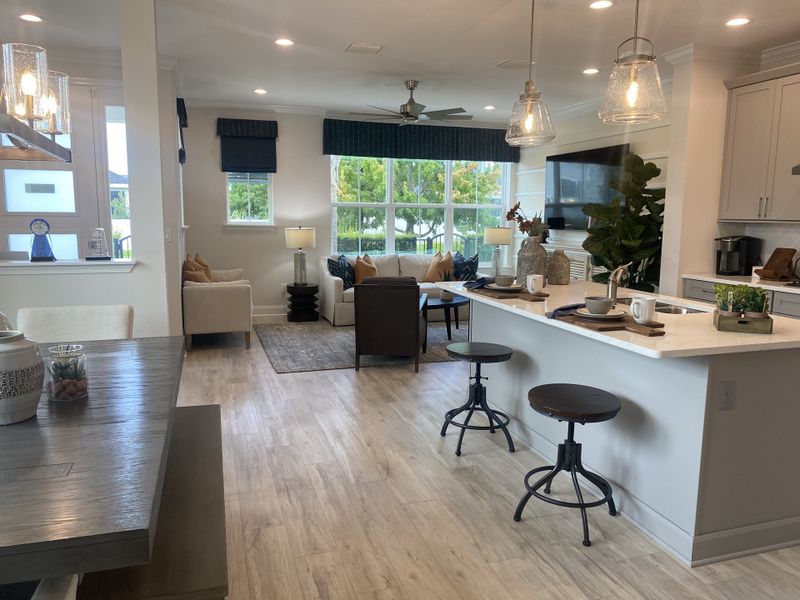 An open-plan living area with elegant lighting, cozy seating, and a modern kitchen, accented with light wood flooring.