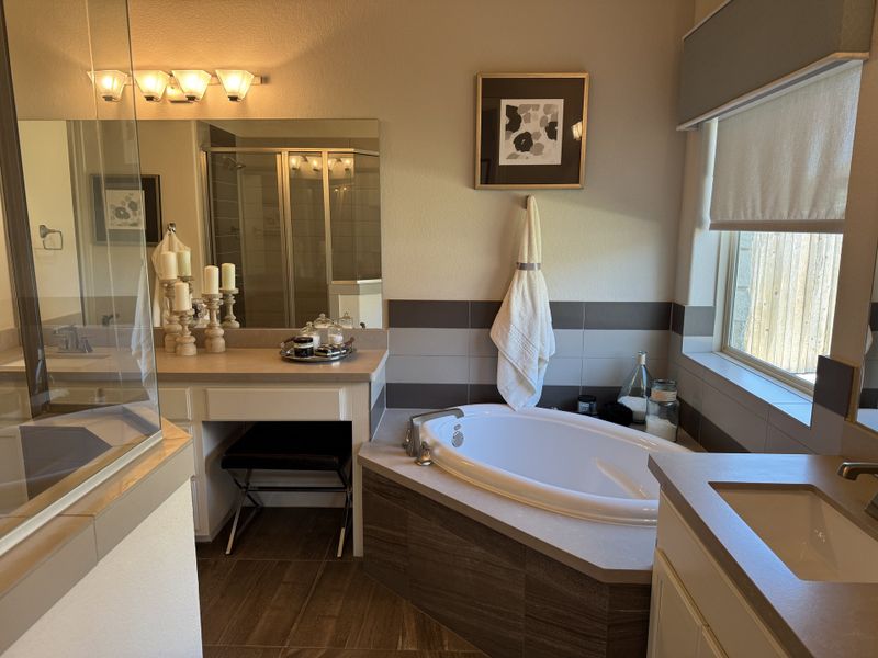 A cozy bathroom featuring a corner tub, elegant candles, spacious counter, and natural light through a large window.