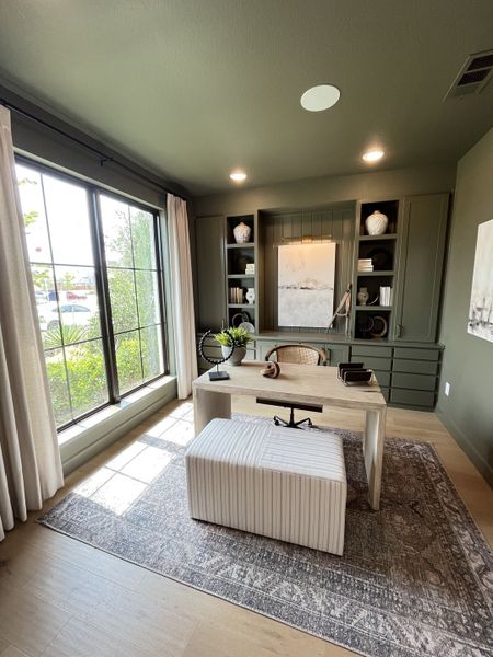 A chic home office with built-in shelves, large window, modern desk, and cozy seating on a patterned rug.