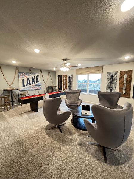 A cozy entertainment room featuring modern gray swivel chairs, a round table, and a shuffleboard game.
