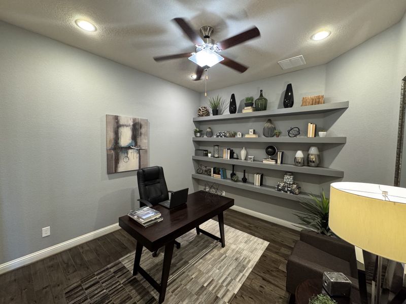 A sleek home office featuring dark wood floors, a modern desk, artful shelving, and ambient lighting for a productive atmosphere.