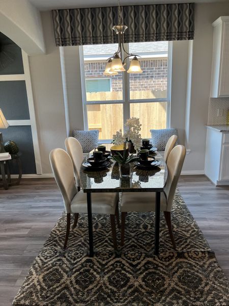 A chic dining area with a patterned rug, elegant table setting, and natural light from a large window. A chic dining area with a patterned rug, elegant table setting, and natural light from a large window.