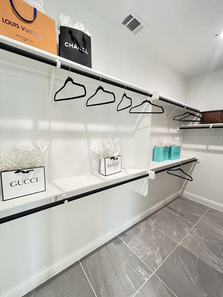 A spacious walk-in closet with sleek black hangers, luxury shopping bags, and elegant gray tile flooring.