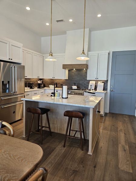 A modern kitchen with a marble island, sleek cabinetry, pendant lighting, and hardwood floors.