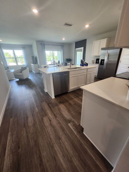 A modern kitchen with sleek cabinetry, stainless appliances, and open layout, featuring wood flooring and ample natural light.
