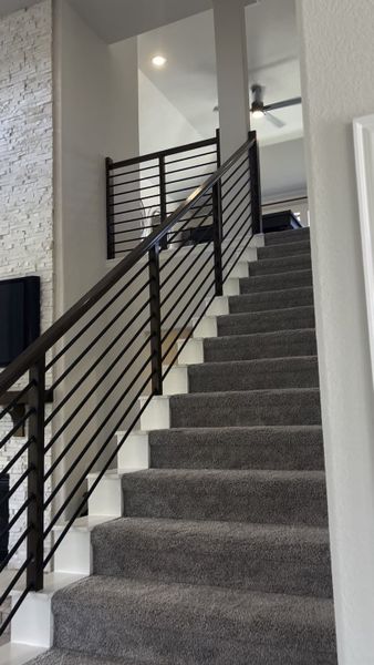 A modern staircase with plush carpeting, sleek metal railing, and stacked stone accent wall, offering an elegant touch.