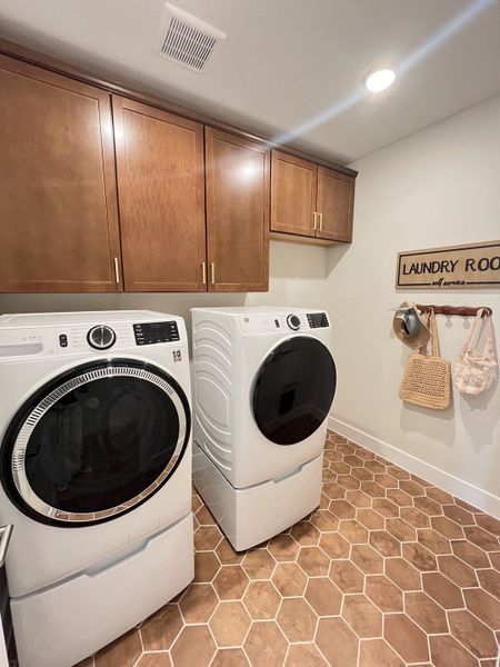 A modern laundry room with sleek appliances, wooden cabinets, and hexagonal floor tiles.