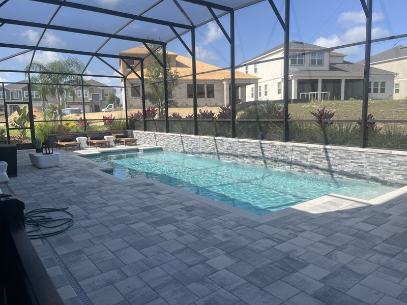 A stylish outdoor area with a screened pool and stone accents, offering sunlit seating and a vibrant garden view. A stylish outdoor area with a screened pool and stone accents, offering sunlit seating and a vibrant garden view.