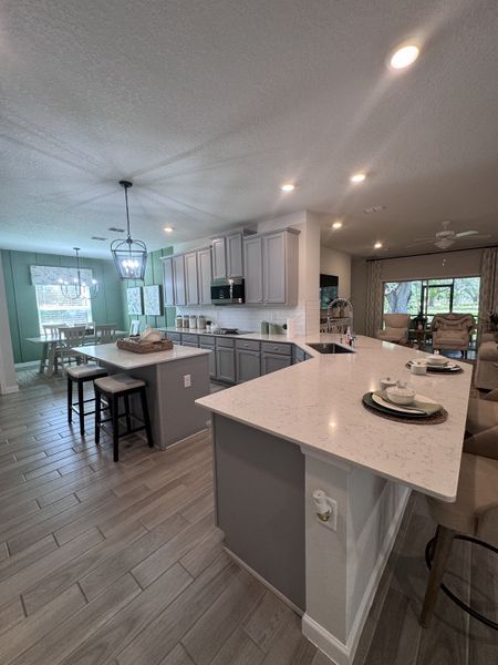 A modern kitchen with sleek gray cabinets, a spacious island, and elegant dining area, featuring chic lighting and tiled floors.