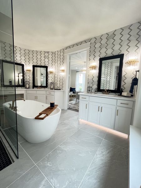 A modern bathroom featuring a freestanding tub, geometric wall patterns, dual sinks, and elegant lighting.