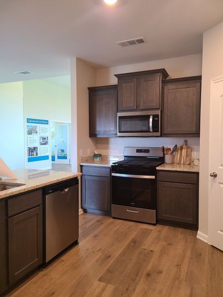 A modern kitchen with dark wood cabinets, granite countertops, stainless steel appliances, and sleek wood flooring. A modern kitchen with dark wood cabinets, granite countertops, stainless steel appliances, and sleek wood flooring.