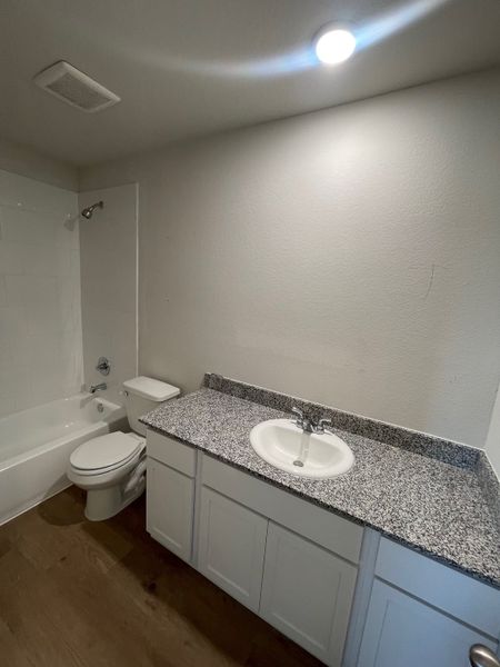 A modern bathroom with a cozy bathtub, granite countertop, and sleek white cabinetry for a clean and inviting look.