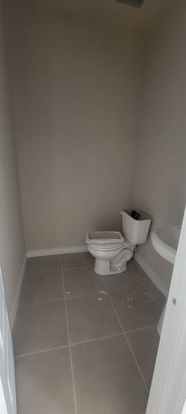 A minimal bathroom with beige walls, tiled floor, and a simple white toilet and sink setup.