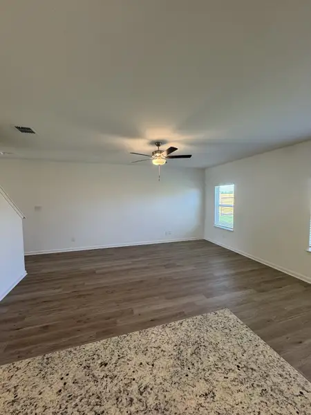 An open-concept living area with wood flooring, white walls, and a ceiling fan, viewed from a granite countertop.