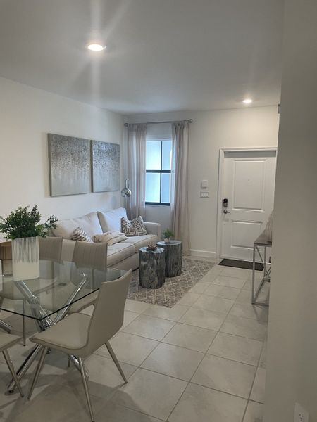 A cozy living area featuring a plush sofa, modern decor, and a glass dining table on tiled flooring.