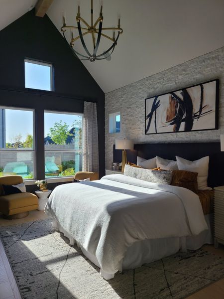 A modern bedroom featuring a vaulted ceiling, elegant chandelier, and natural light streaming through large windows.