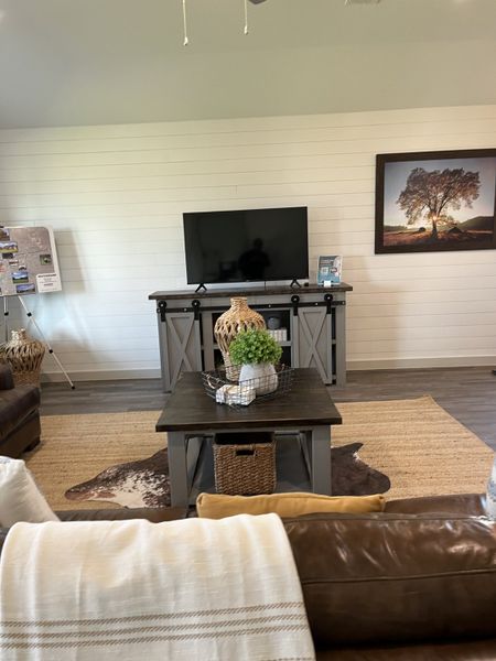 A cozy living room with a shiplap wall, TV console, rustic coffee table, and leather sofas. Warm and inviting decor.