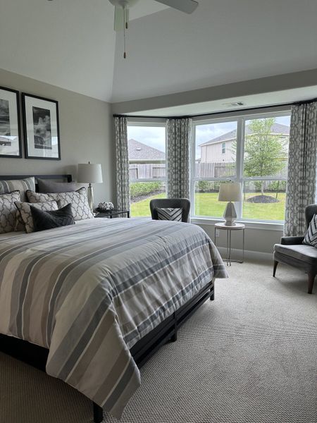 A cozy bedroom with a striped bedspread, large windows, and elegant gray chairs creating a serene ambiance. A cozy bedroom with a striped bedspread, large windows, and elegant gray chairs creating a serene ambiance.