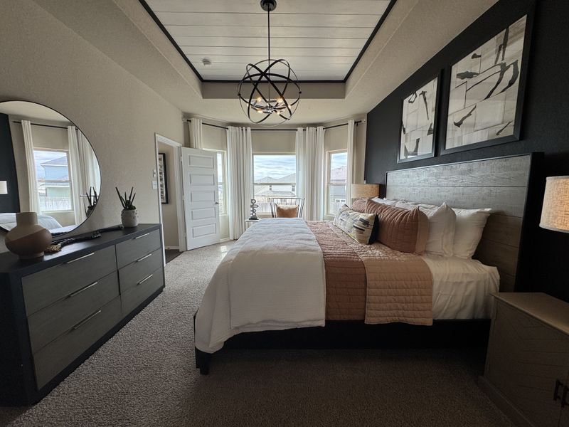 A cozy bedroom with a modern chandelier, abstract art, and natural light enhancing the elegant decor.