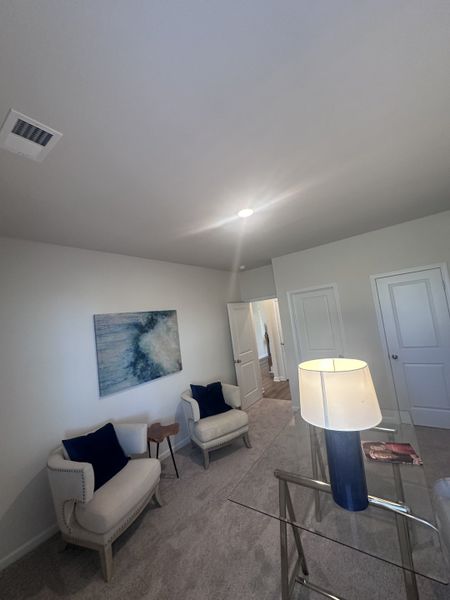 A cozy room with elegant chairs, modern art, and a sleek glass desk, complemented by soft lighting and plush carpeting.