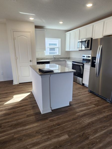 A modern kitchen featuring sleek white cabinetry, granite countertops, stainless steel appliances, and warm hardwood flooring.