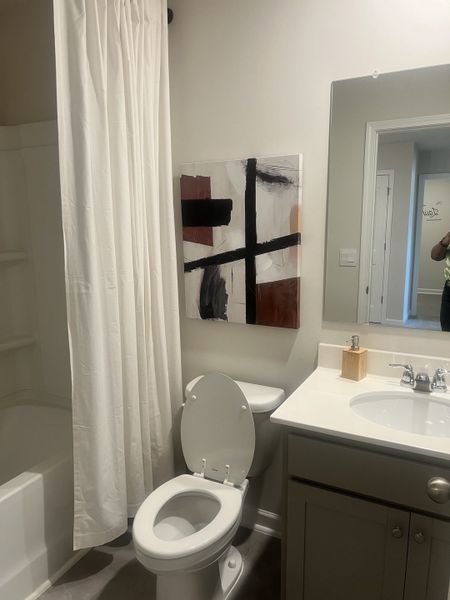 A modern bathroom featuring a clean white aesthetic, shower-tub combo, abstract wall art, and sleek vanity.