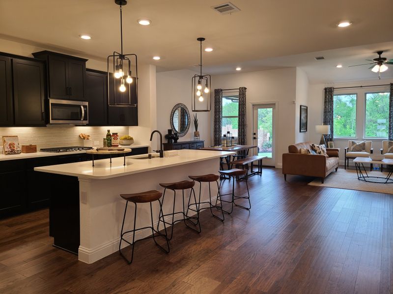 A modern open-plan kitchen and living area with dark cabinetry, a large island, stylish pendant lighting, and a cozy seating space. A modern open-plan kitchen and living area with dark cabinetry, a large island, stylish pendant lighting, and a cozy seating space.