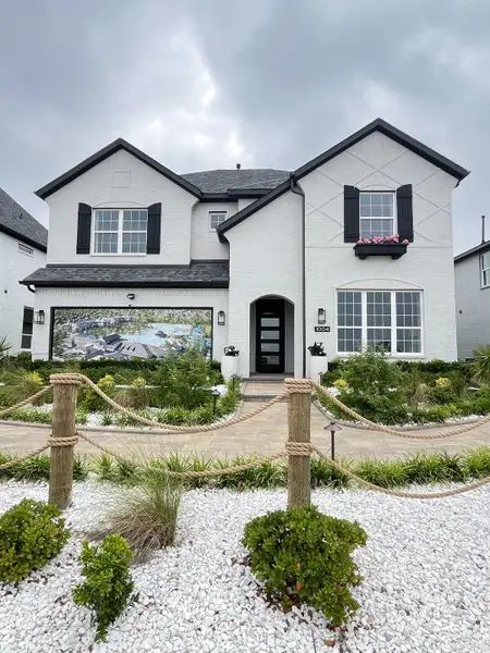 A charming white brick home with black shutters and a lush garden in Bellagio by Megatel Homes (Forney, TX).