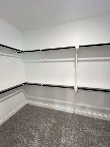 A spacious walk-in closet with sleek black shelving and plush gray carpet flooring.
