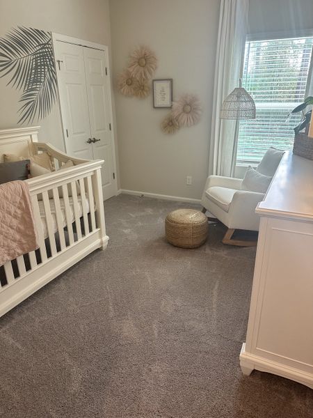 A cozy nursery with soft carpeting, a white crib, a comfy chair, and charming wall decor featuring floral accents.