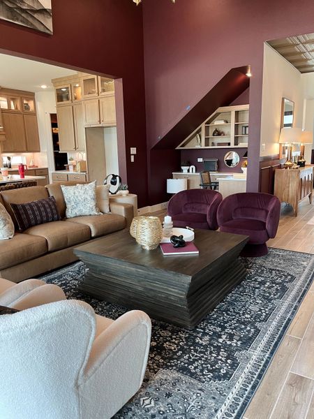 A cozy living room with rich maroon walls, modern furniture, and an elegant open plan leading to a chic kitchen.