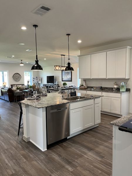 A modern kitchen with a central island, sleek granite countertops, pendant lighting, and open concept living area.