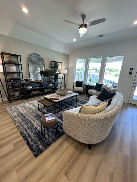 A cozy living room with a curved sofa, stylish shelves, and large windows, complemented by modern decor and a ceiling fan.