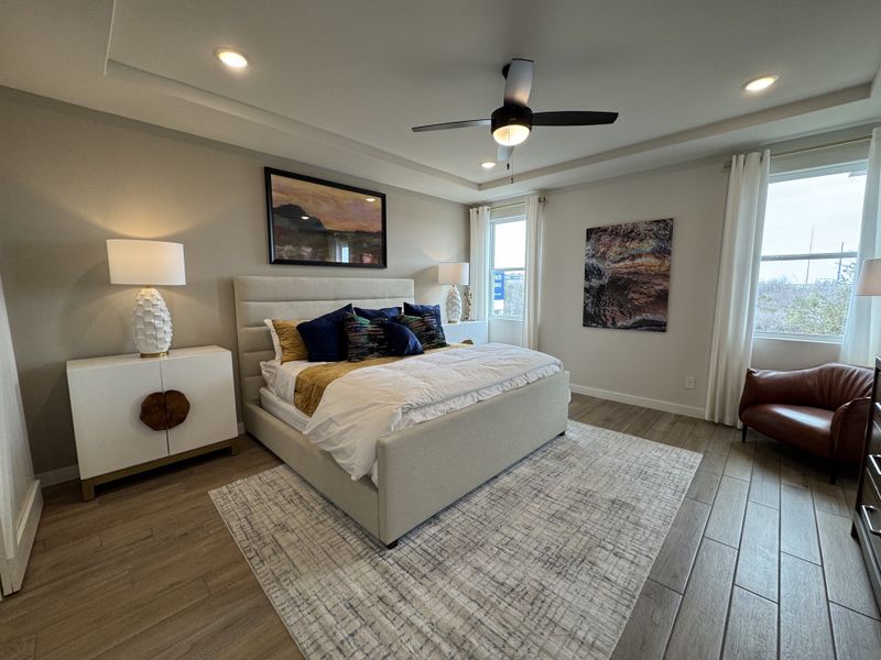 A modern bedroom with chic decor, featuring a cozy bed, elegant lighting, plush seating, and sleek wooden flooring.