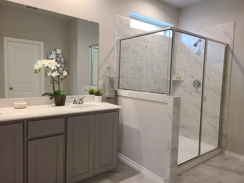 A contemporary bathroom featuring a sleek gray vanity, floral decor, and a spacious glass-enclosed shower.