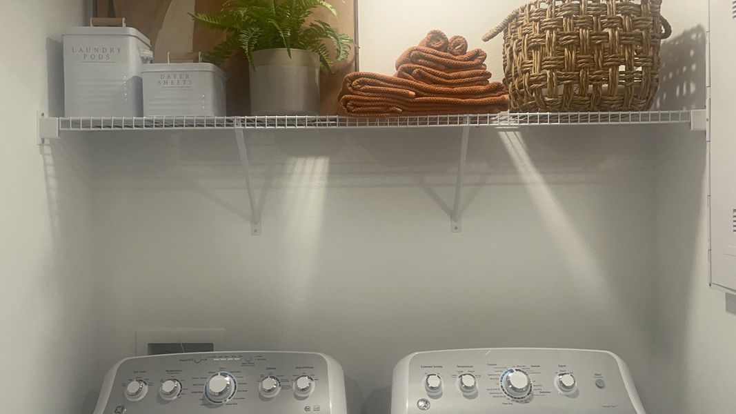 A well-organized laundry room with modern appliances, open shelving, and neatly stacked towels.