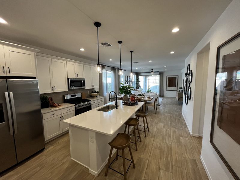 Open-concept kitchen with white cabinets, pendant lights, and a spacious island leading into a bright living area.