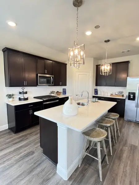 A modern kitchen with dark wood cabinets, sleek white countertops, and stylish pendant lighting above a central island. A modern kitchen with dark wood cabinets, sleek white countertops, and stylish pendant lighting above a central island.
