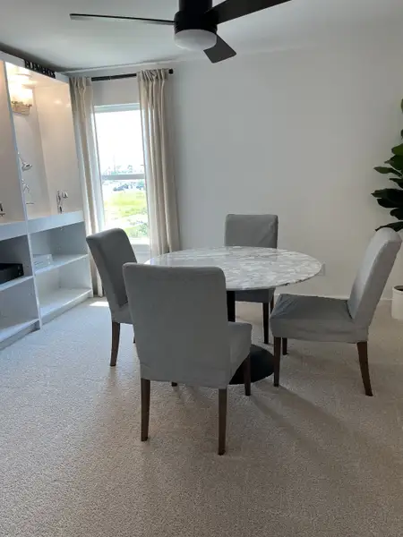 A cozy dining area with a round marble table, gray chairs, and large window, creating a bright and inviting space.