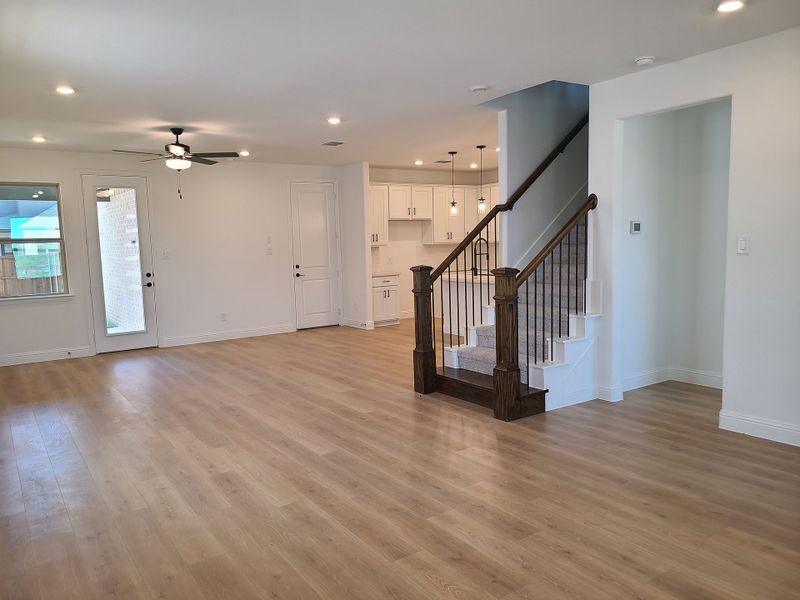 A spacious open-concept living area with light wood floors, modern fixtures, and a chic staircase leading upstairs.