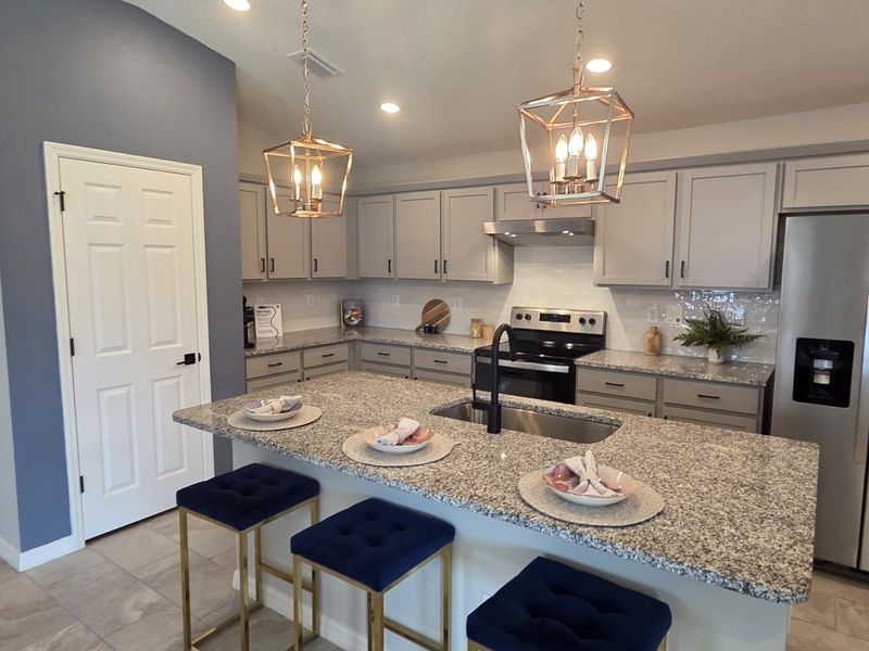 A modern kitchen with granite countertops, sleek gray cabinets, and elegant pendant lighting.