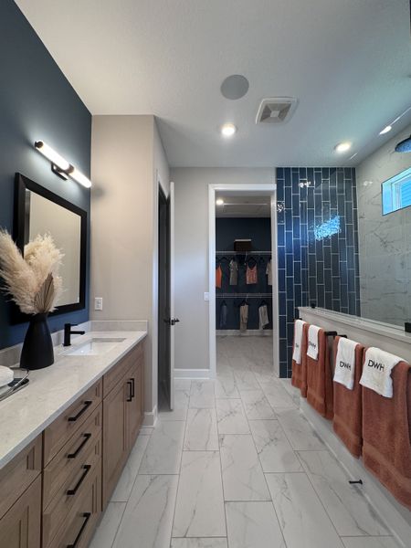 Modern bathroom with a sleek wooden vanity, navy accent wall, and marble tile flooring leading to a spacious walk-in closet.