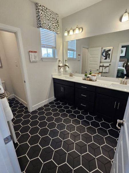 A modern bathroom with geometric floor tiles, dual sinks, and contemporary lighting.